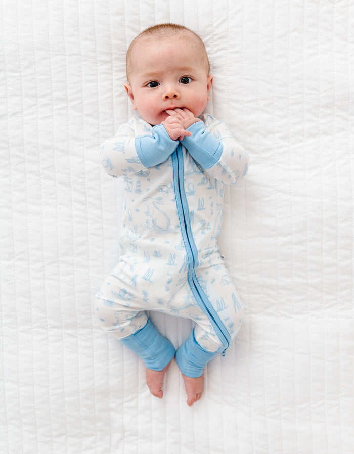 Baby wearing a white and blue Easter bamboo romper on a white textured surface