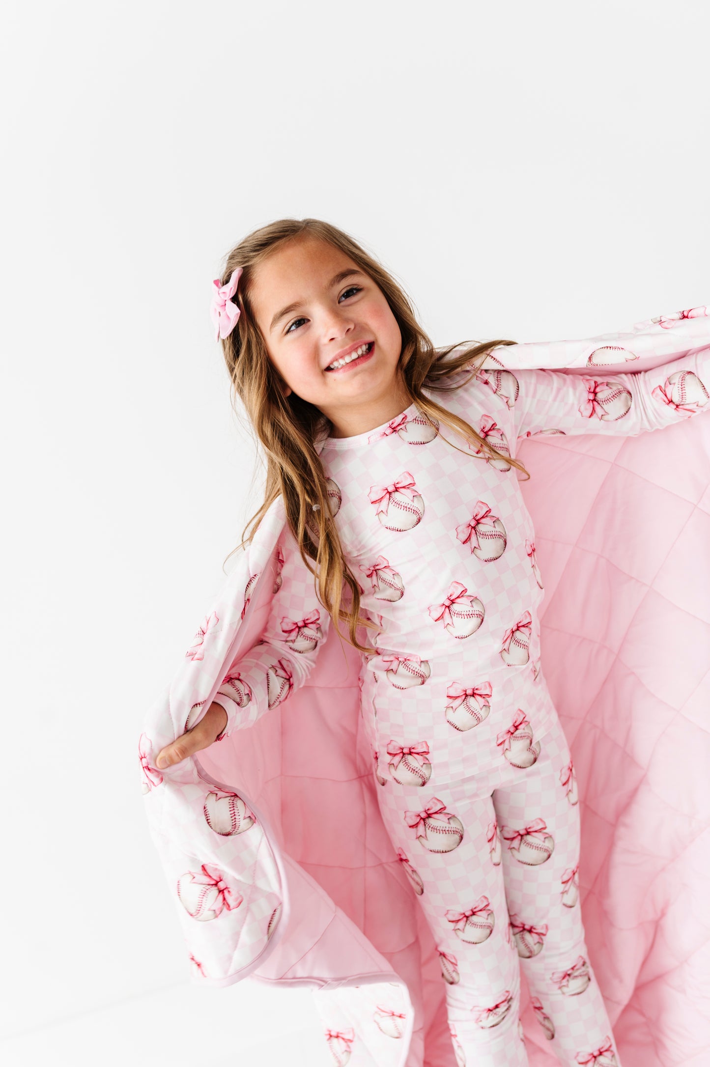 Young girl wearing a pink and white bamboo baseball two-piece set, wrapped in a matching bamboo blanket