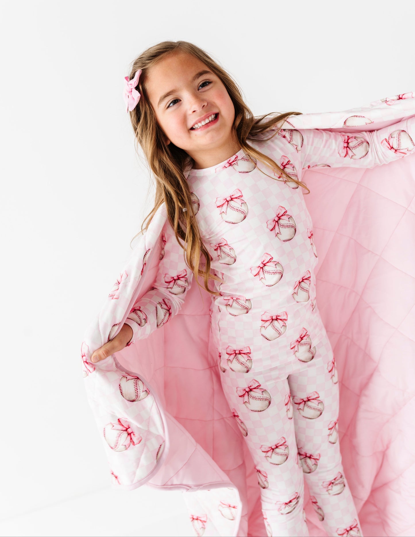 Young girl wearing pink and white bamboo baseball pjs with bow patterns on a white background