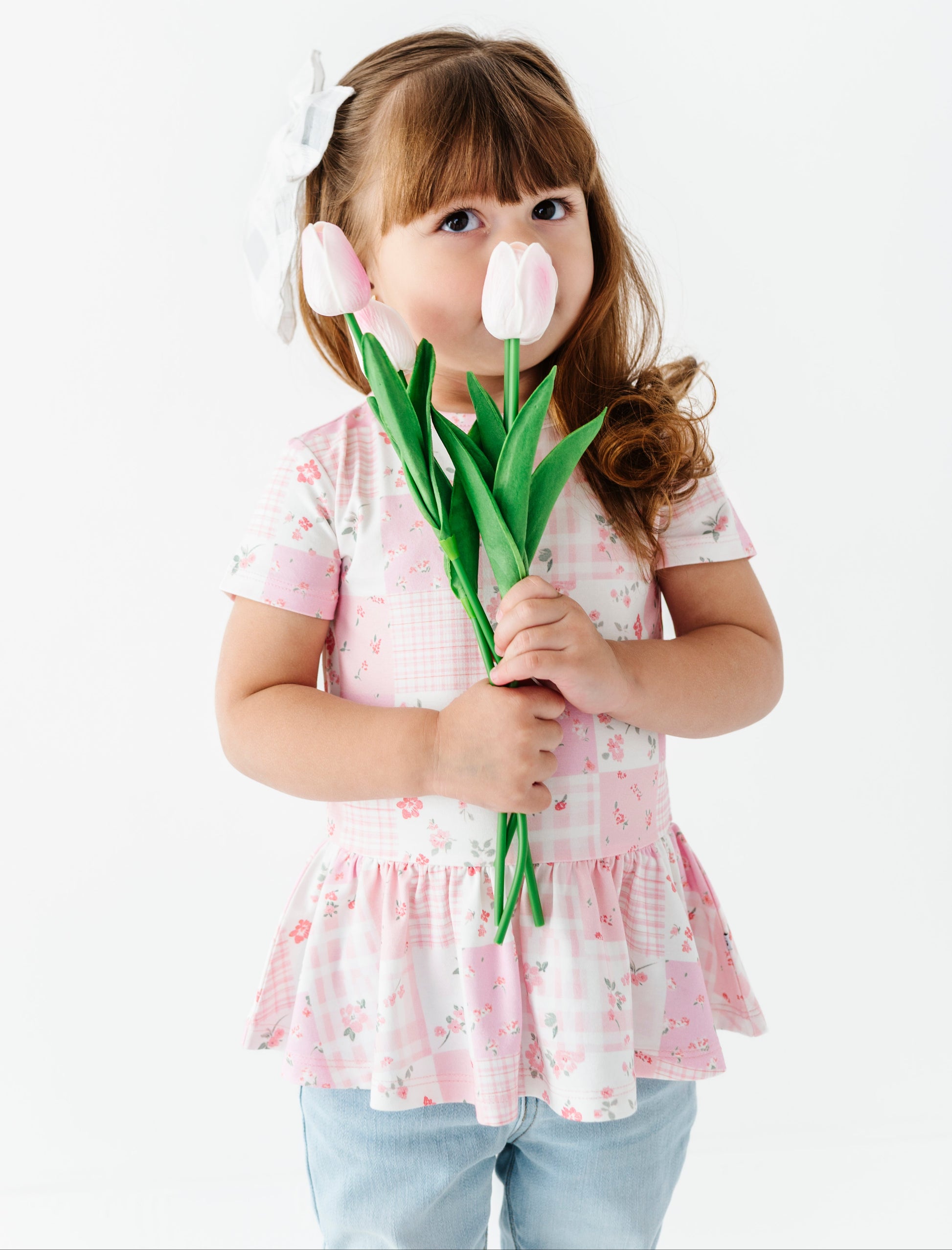 Child holding a bouquet of tulips wearing a bamboo-cotton peplum top against a white background
