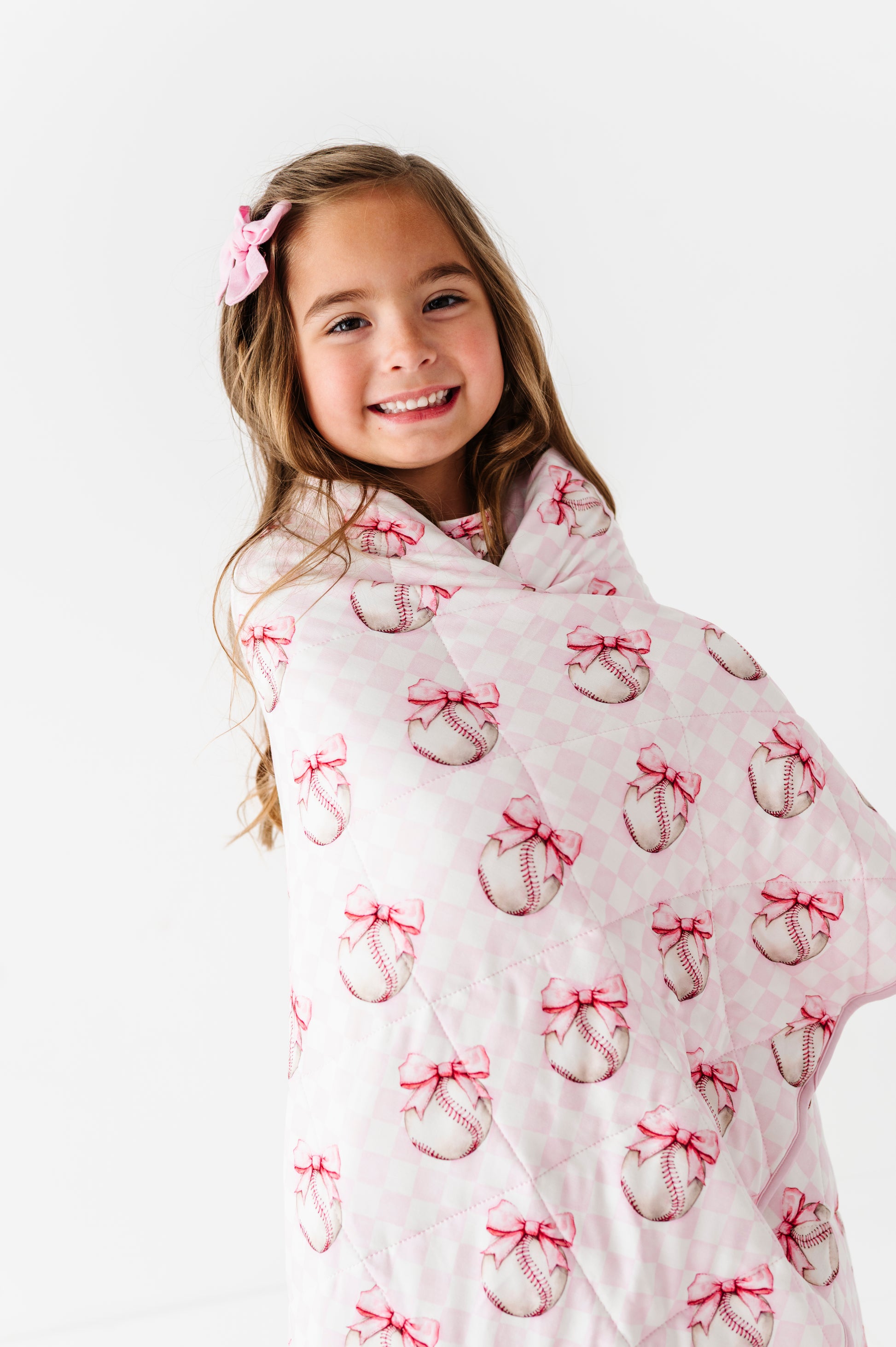 Young girl wrapped in a pink baseball blanket blanket with bow pattern on a white background