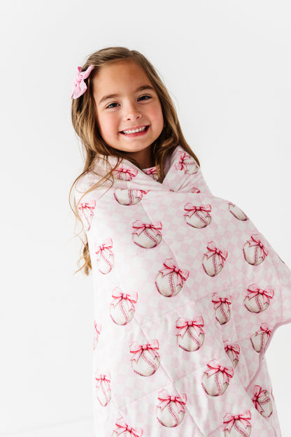 Young girl wrapped in a pink baseball blanket blanket with bow pattern on a white background