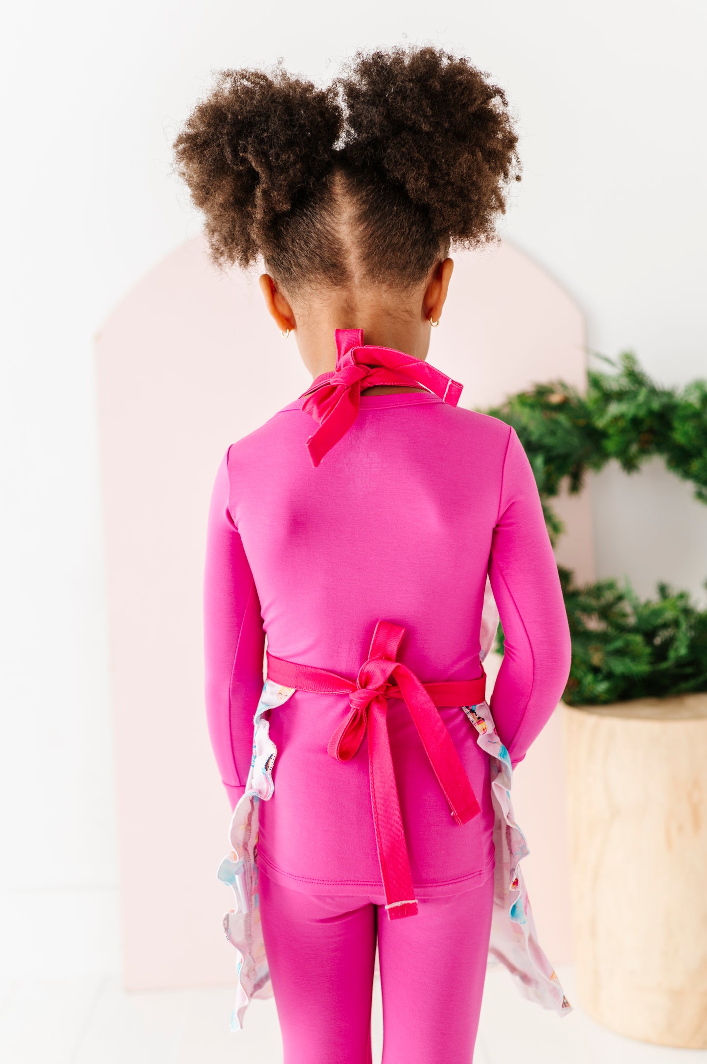 Child wearing a Sugarplum apron tied in the back in two bright pink bows