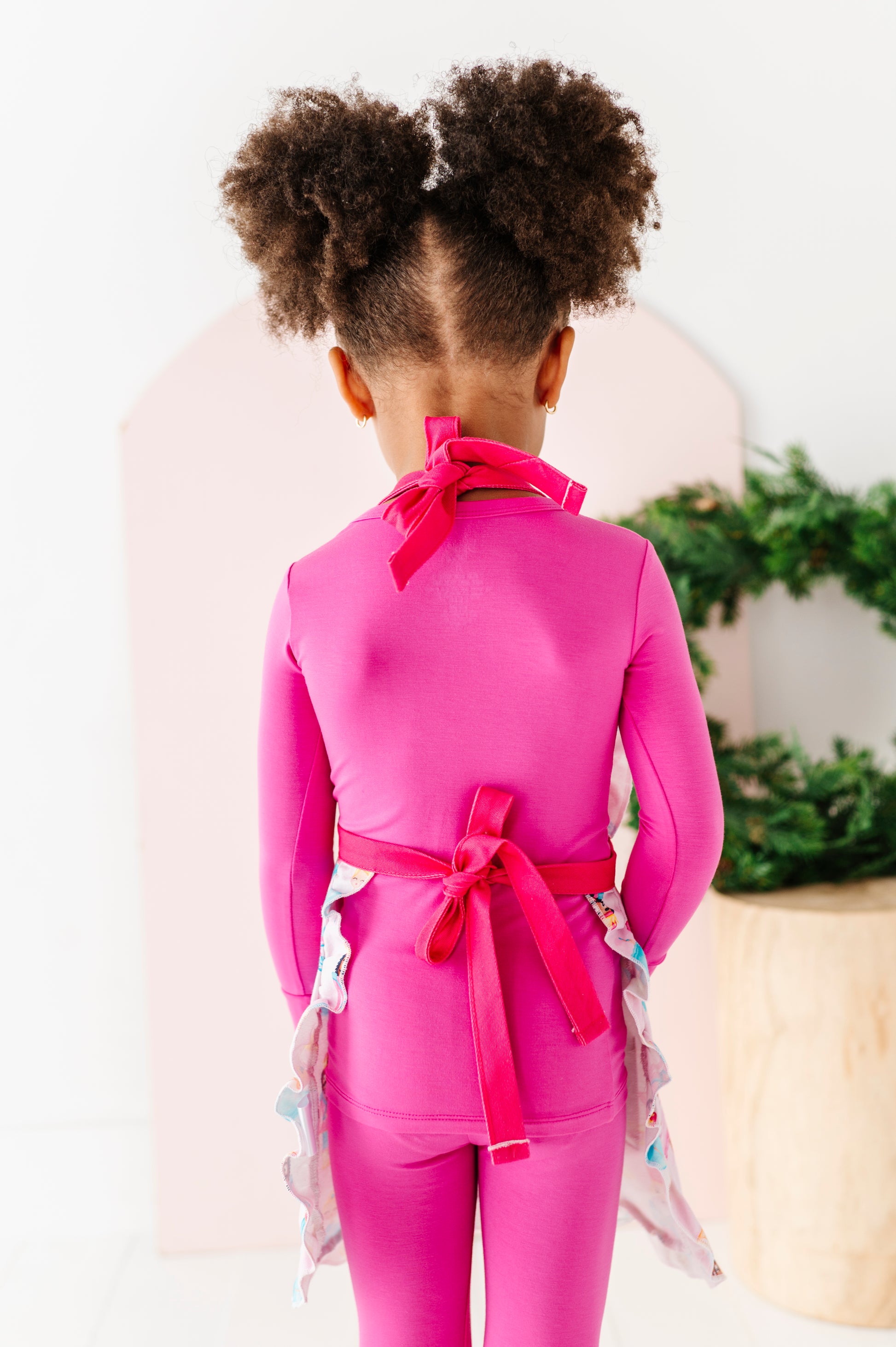 Child wearing a Sugarplum apron tied in the back in two bright pink bows