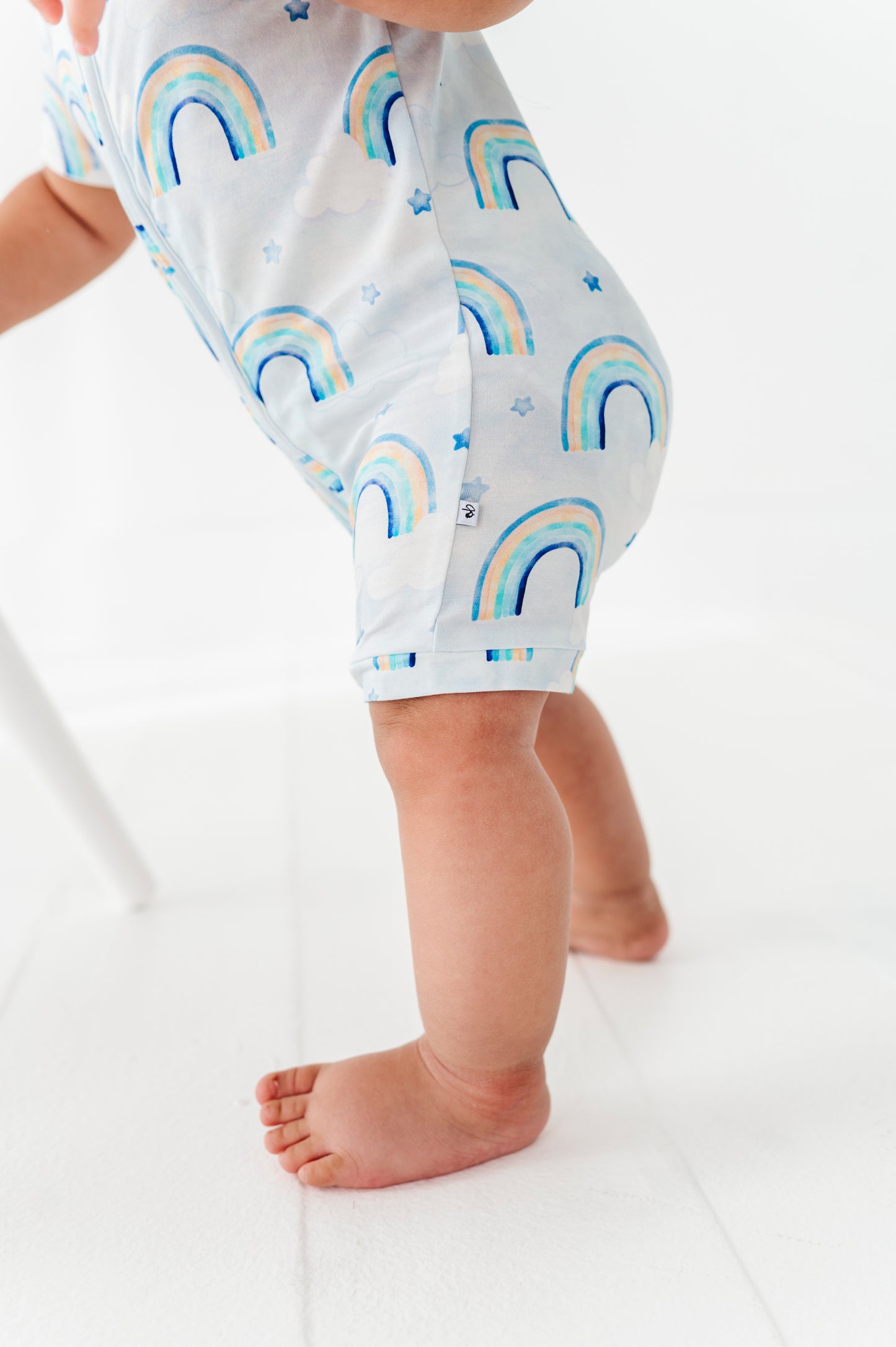 Baby wearing a short romper with rainbow patterns on a white background