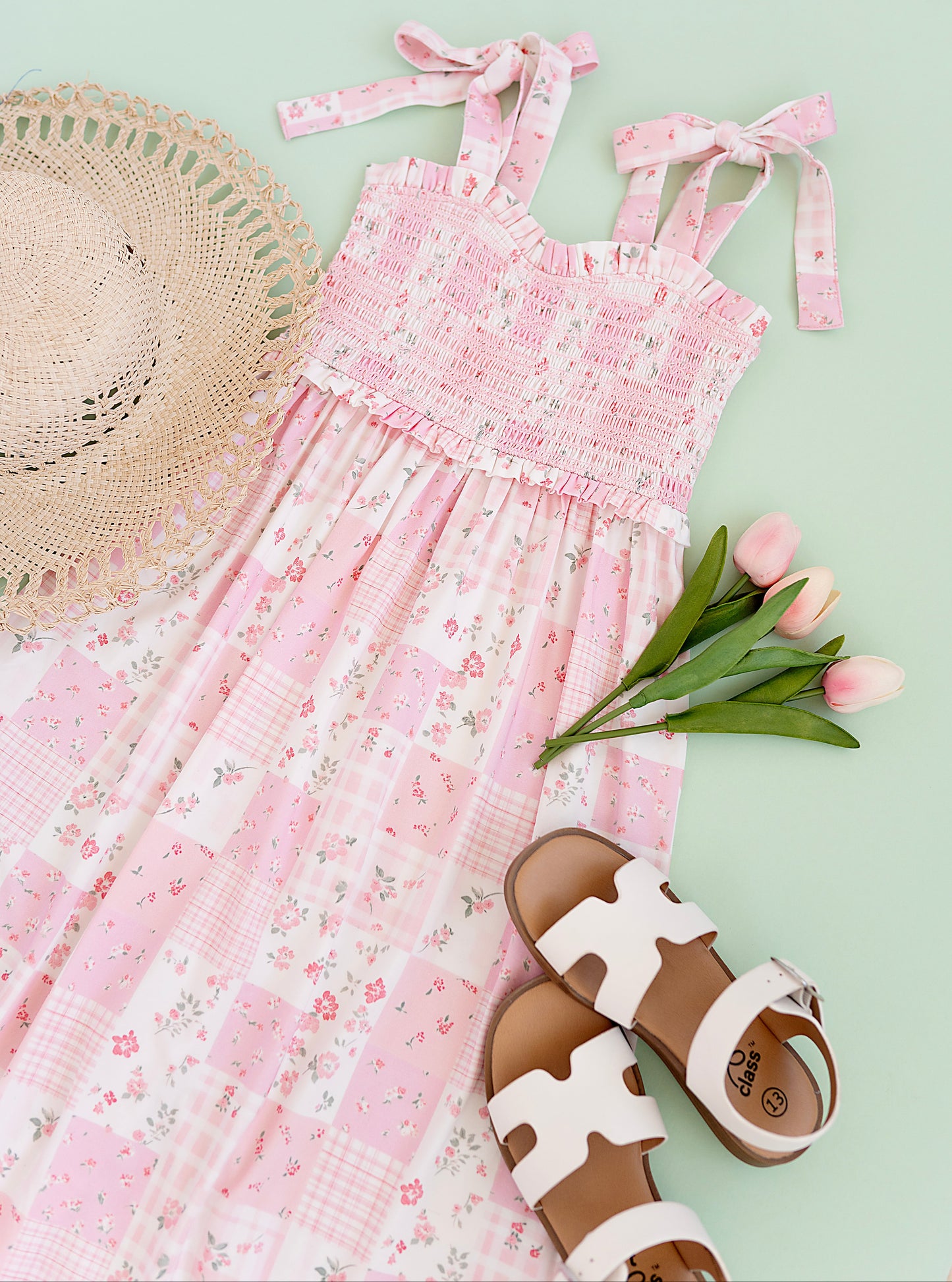 Pink floral maxi dress with matching sandals and a straw hat on a light green background