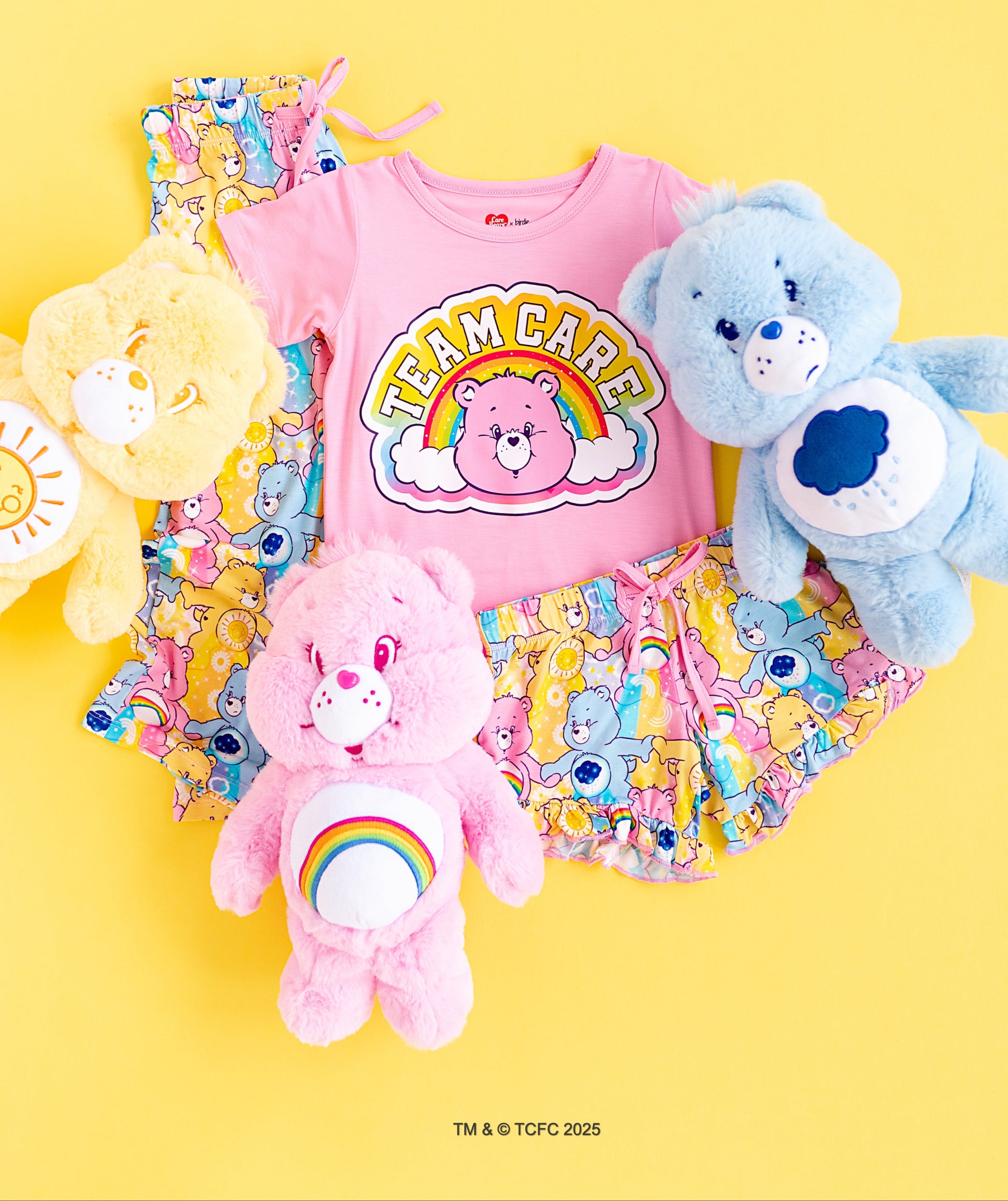 Flat lay of Care Bears™ Stare pajama set with pink t-shirt, printed shorts, pants, and Care Bears plush toys