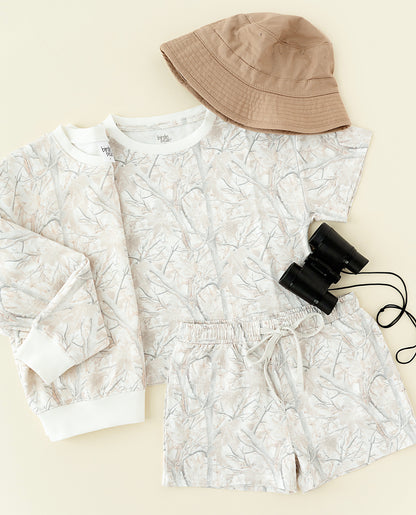 White floral-patterned outfit with a beige bucket hat and black binoculars on a beige background