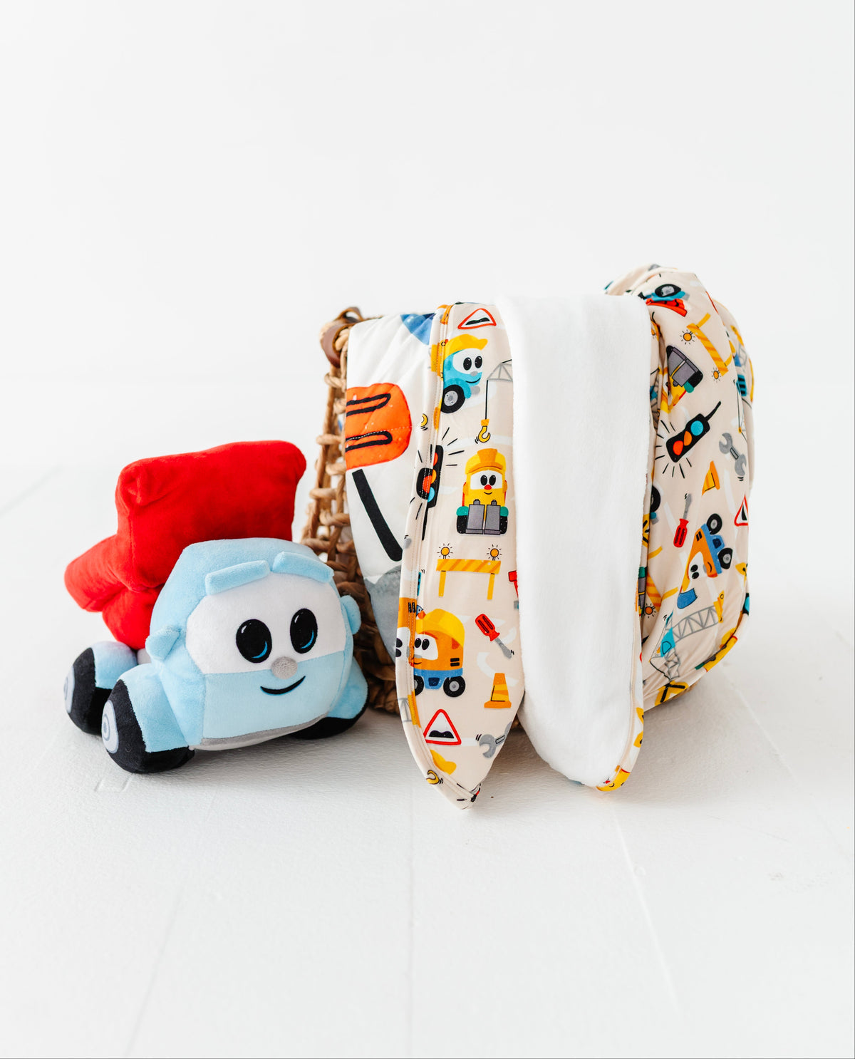 A fabric diaper cover with a colorful construction vehicle print, shown next to a small plush toy truck on a clean white background.