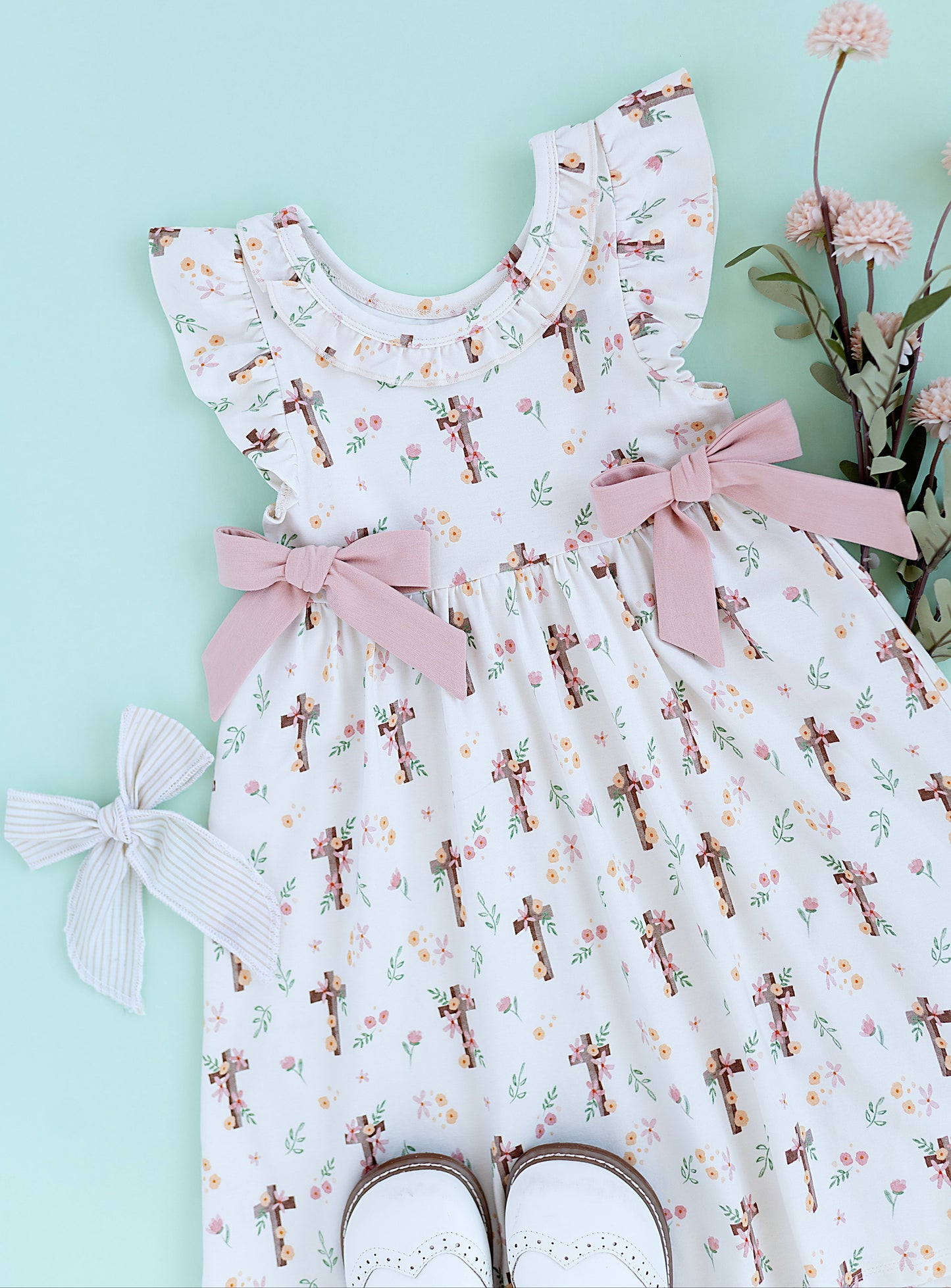 White dress with floral and cross pattern and pink bows on a light blue background