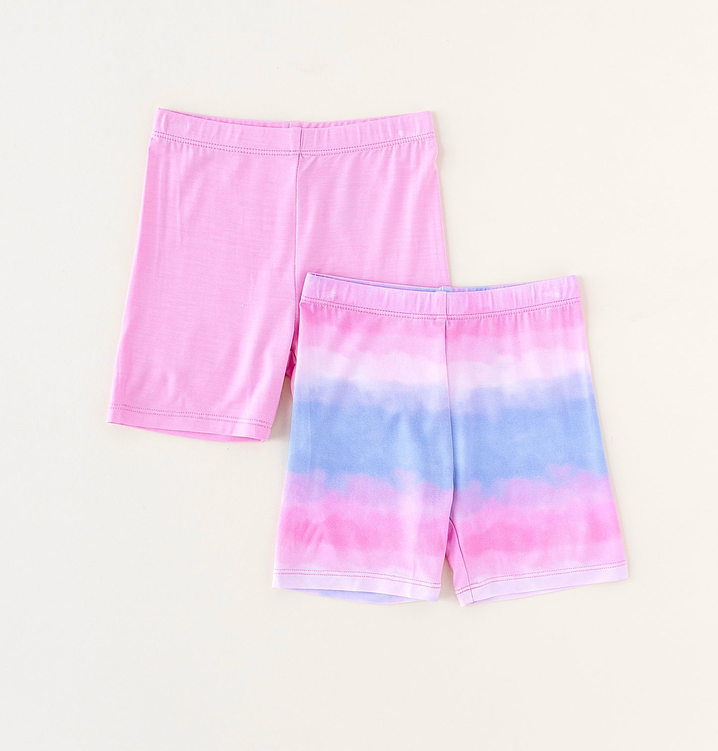 Two pairs of bamboo biker shorts, one solid pink and one tie-dye, on a light beige background.