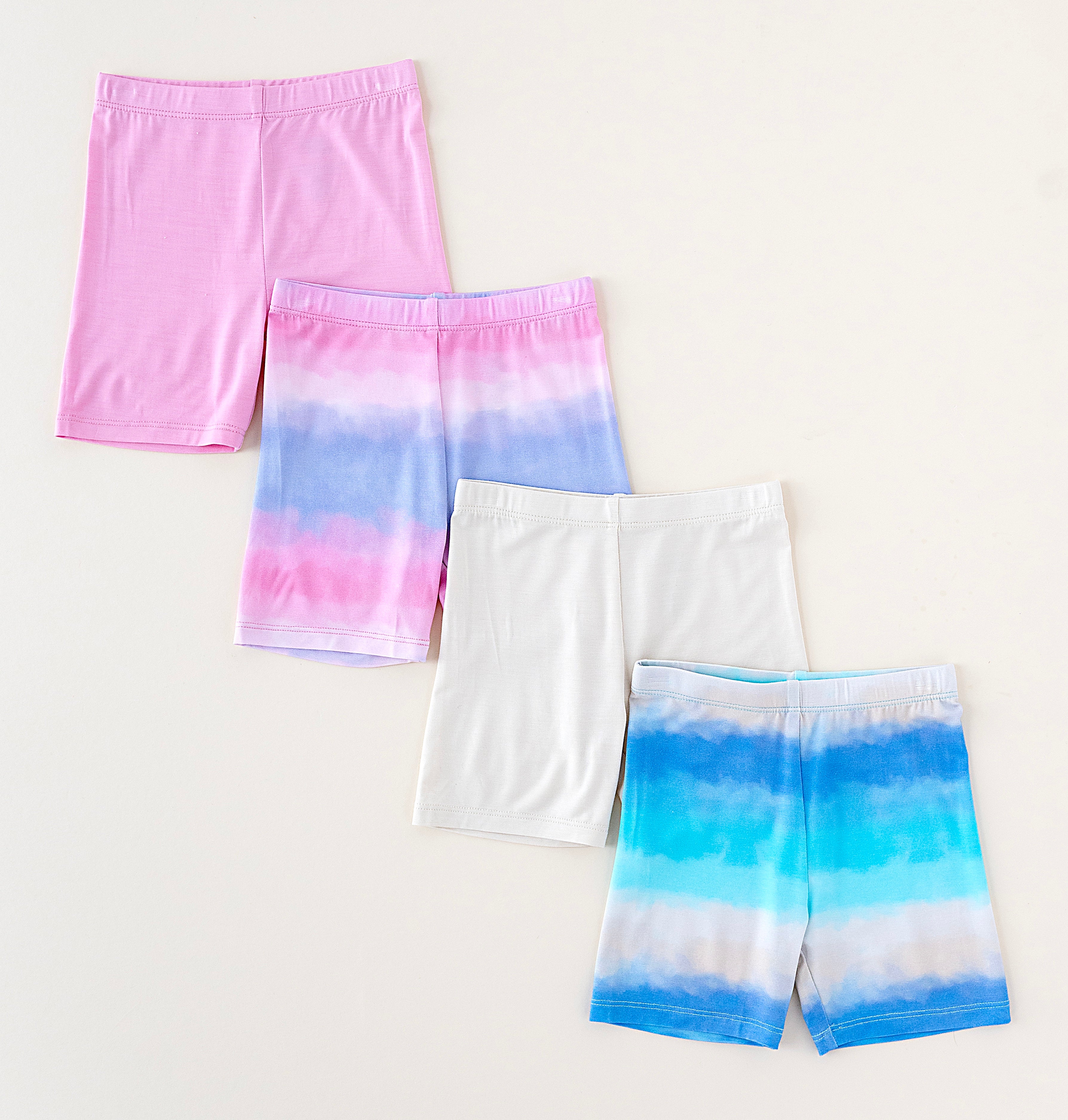 Set of tie-dye bamboo biker shorts in pink, blue, and white on a light gray background