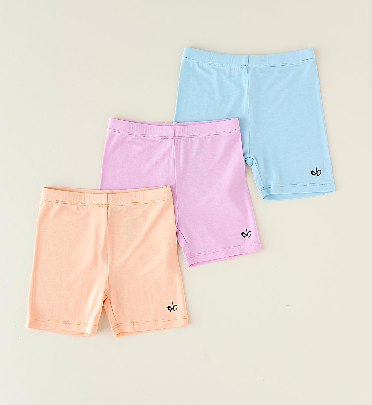Three pairs of pastel-colored bamboo biker shorts on a beige background