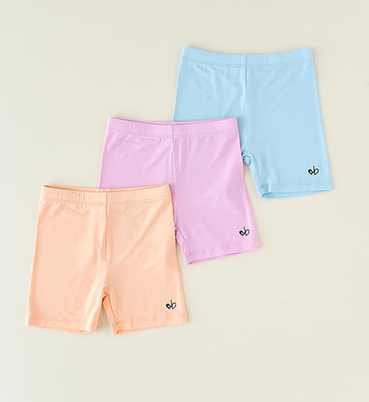 Three pairs of pastel-colored bamboo biker shorts on a beige background