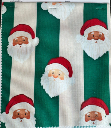 A fabric sample card from Birdie Bean featuring a repeating pattern of Santa Claus faces on green and off-white vertical stripes, photographed on a dark wood surface.