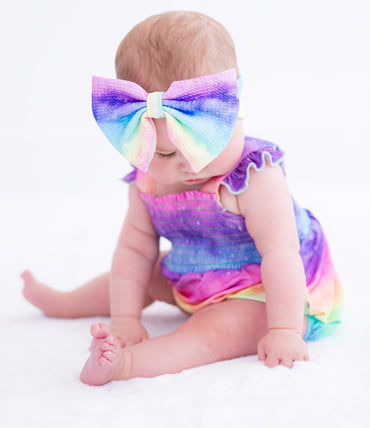 Baby wearing a colorful bow headband with gradient effect on a white background 