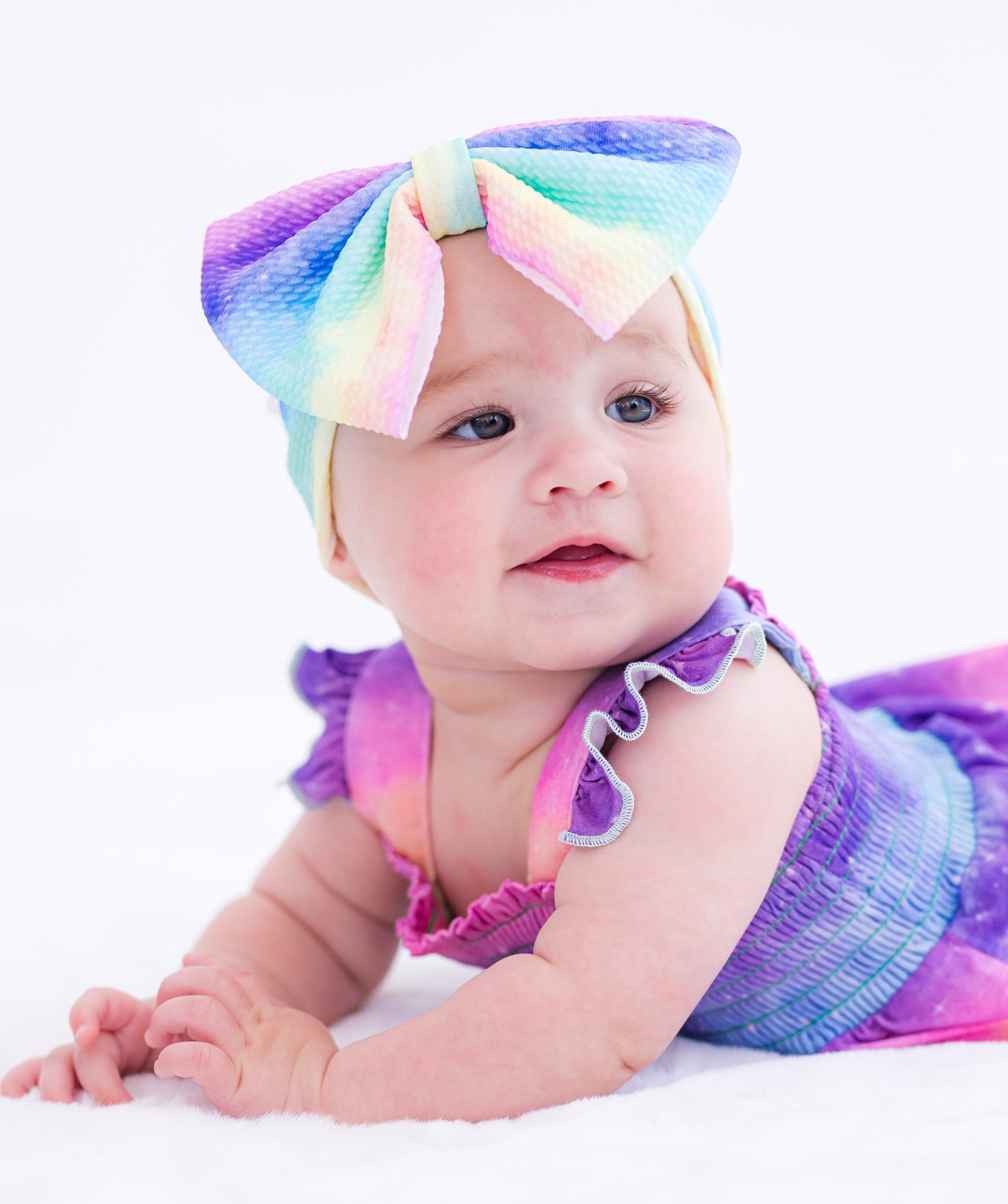 Baby wearing a colorful bow headband with a matching rainbow romper