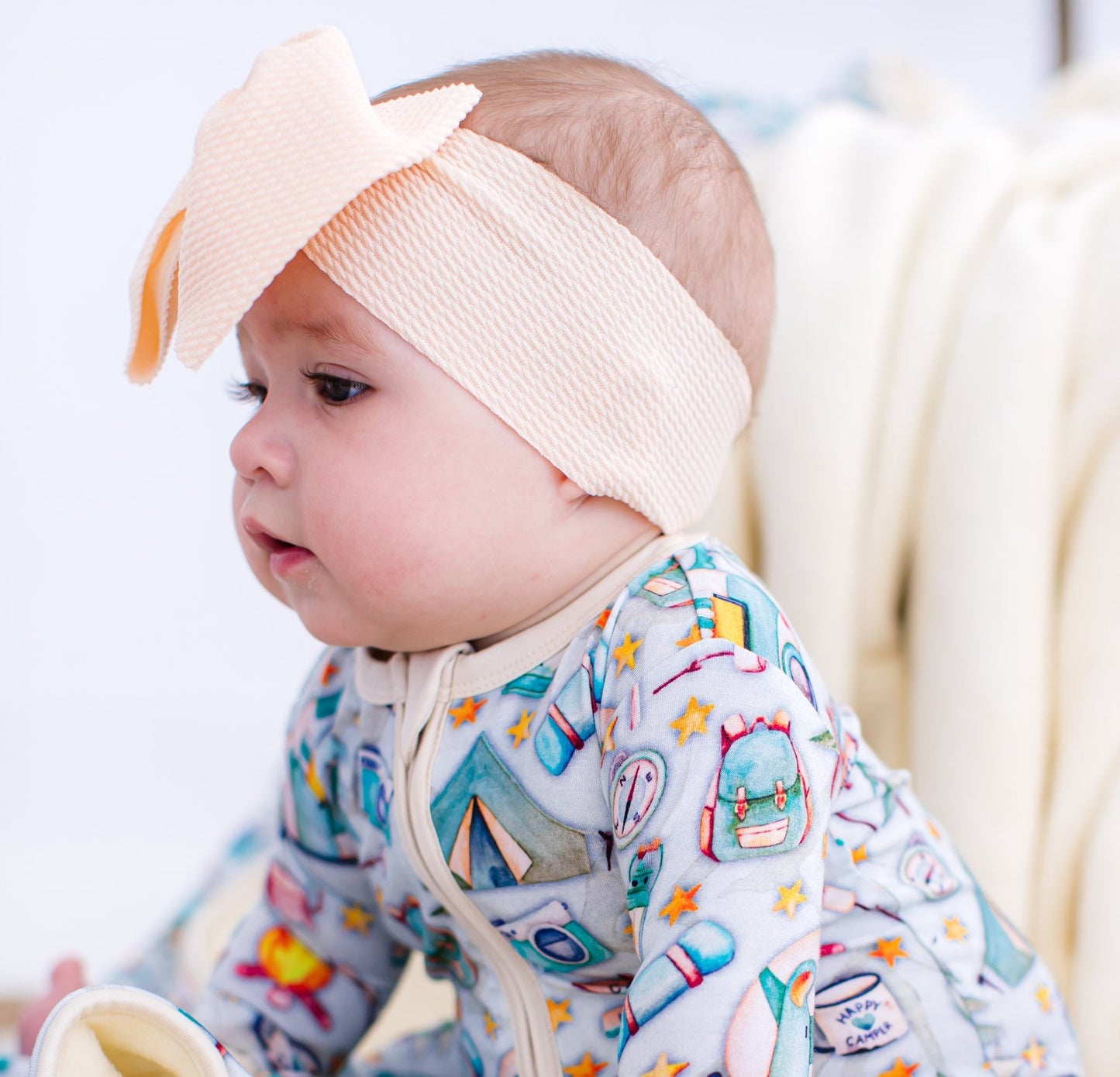 Baby wearing a colorful onesie with cartoon designs and a beige headband.