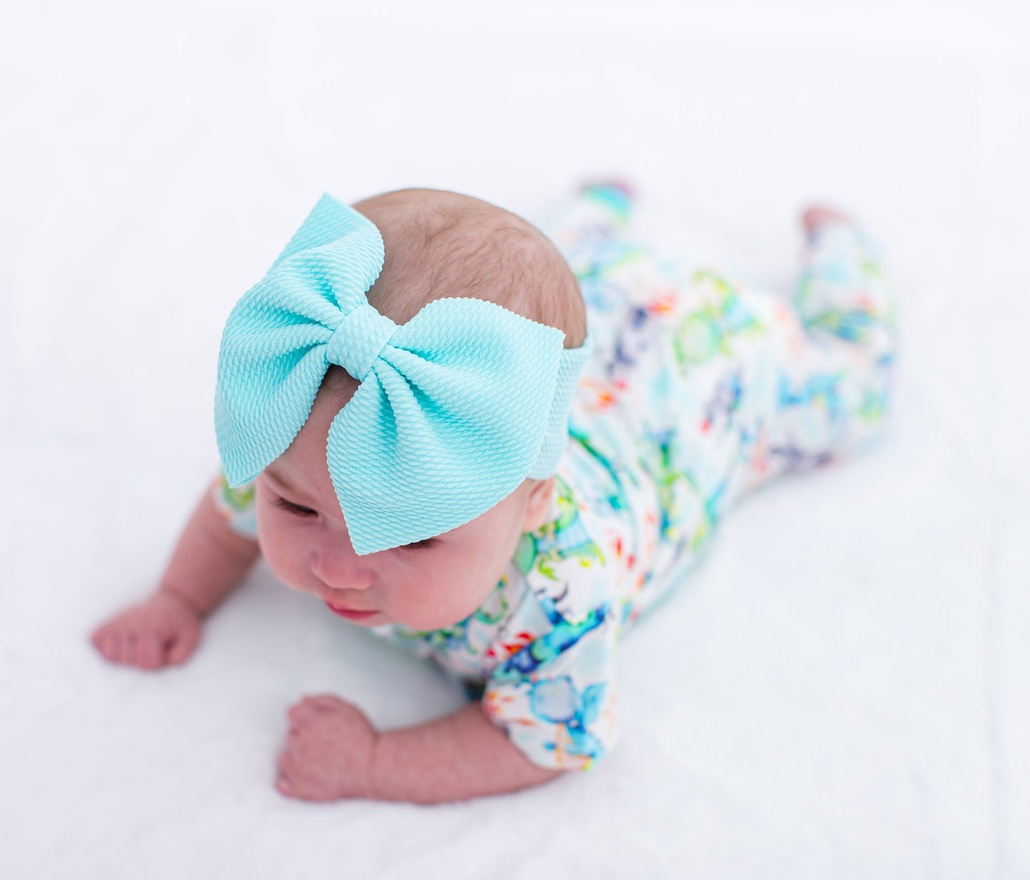 Baby wearing a large sky blue bow headband and colorful outfit on a white background