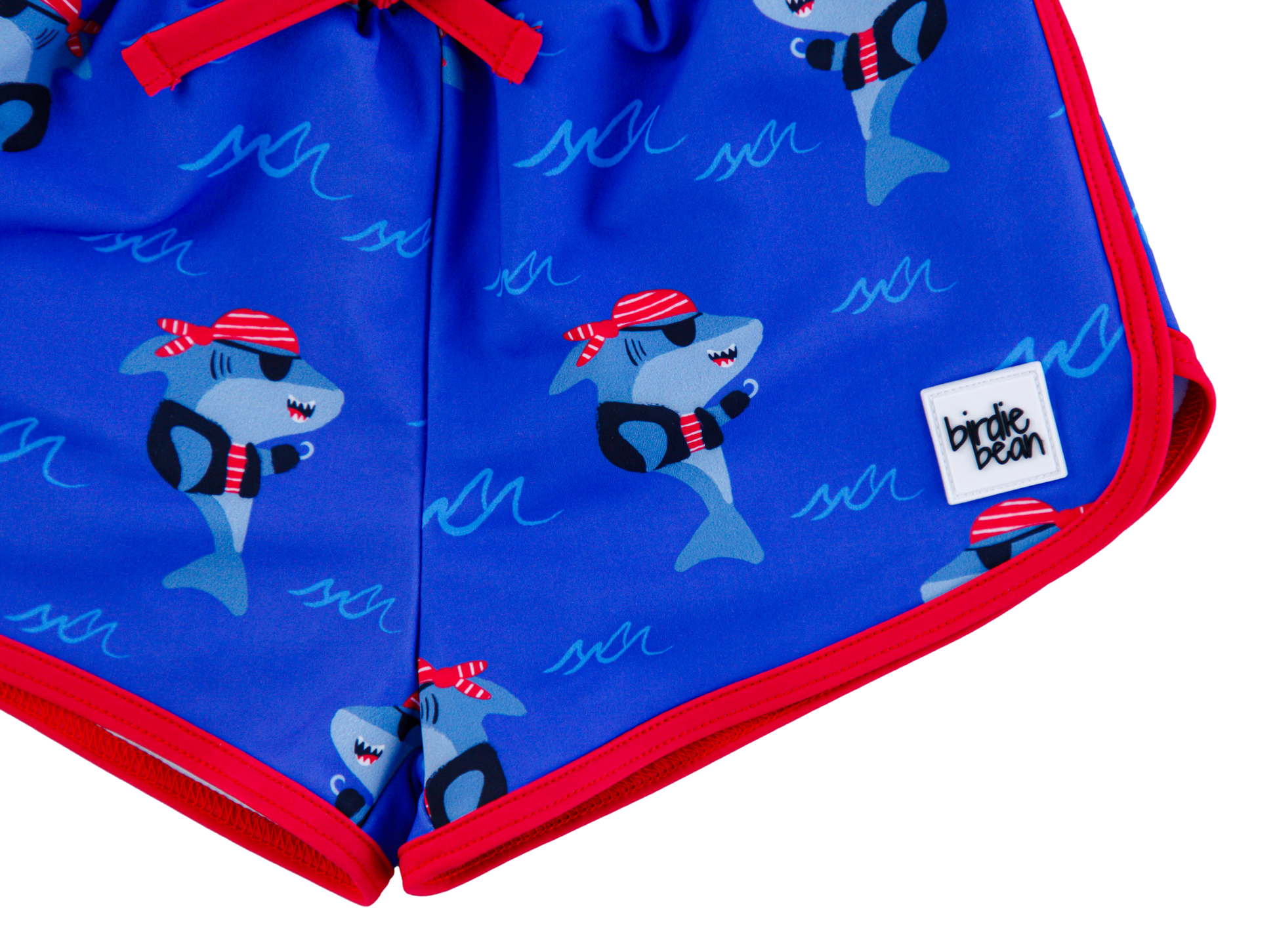 Sebastian Swim Shorties flat lay featuring blue shark print with red trim and small Birdie Bean logo