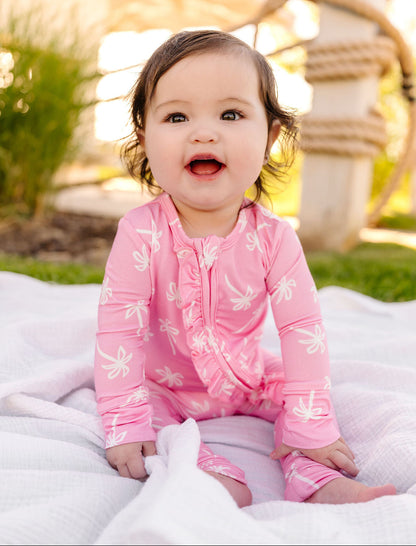 Baby in a pink palm outfit sitting on a blanket outdoors.