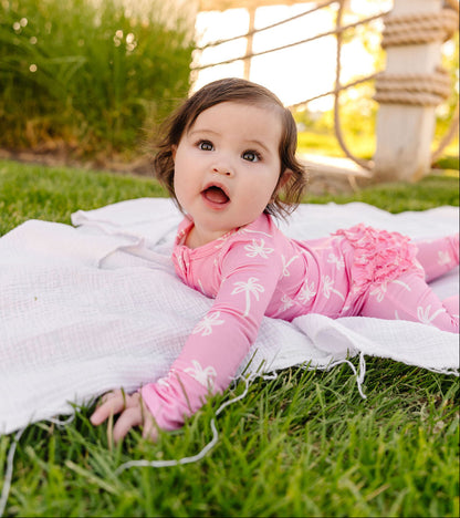 Baby in pink outfit lying on grass with sunset background