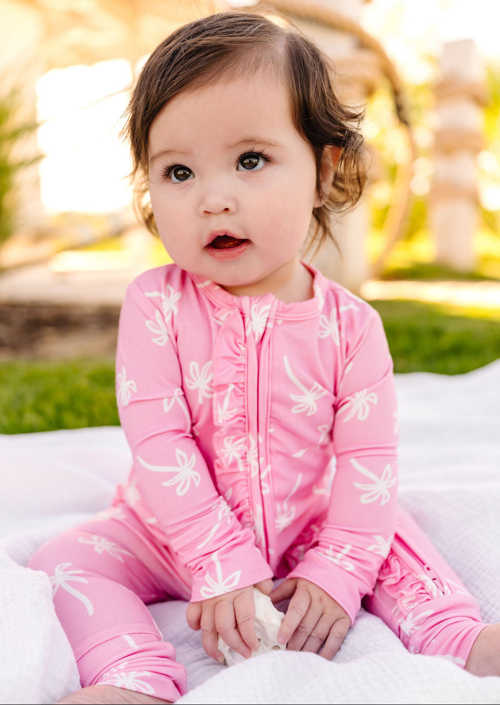 Child wearing a pink outfit with white patterns, sitting outdoors.