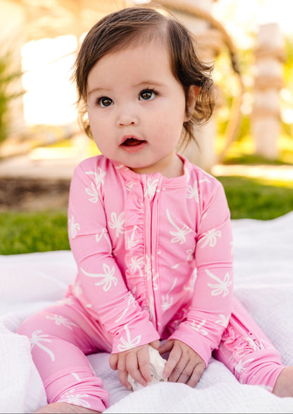 Child wearing a pink outfit with white patterns, sitting outdoors.