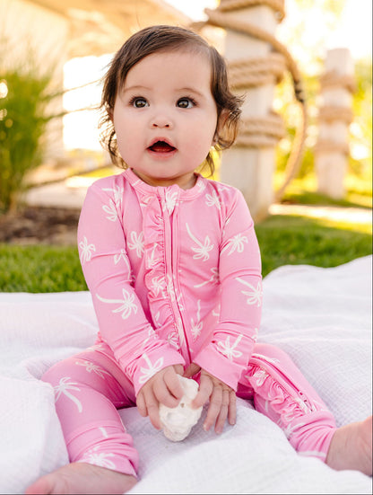 Child wearing a pink outfit with white patterns, sitting on a white blanket outdoors.