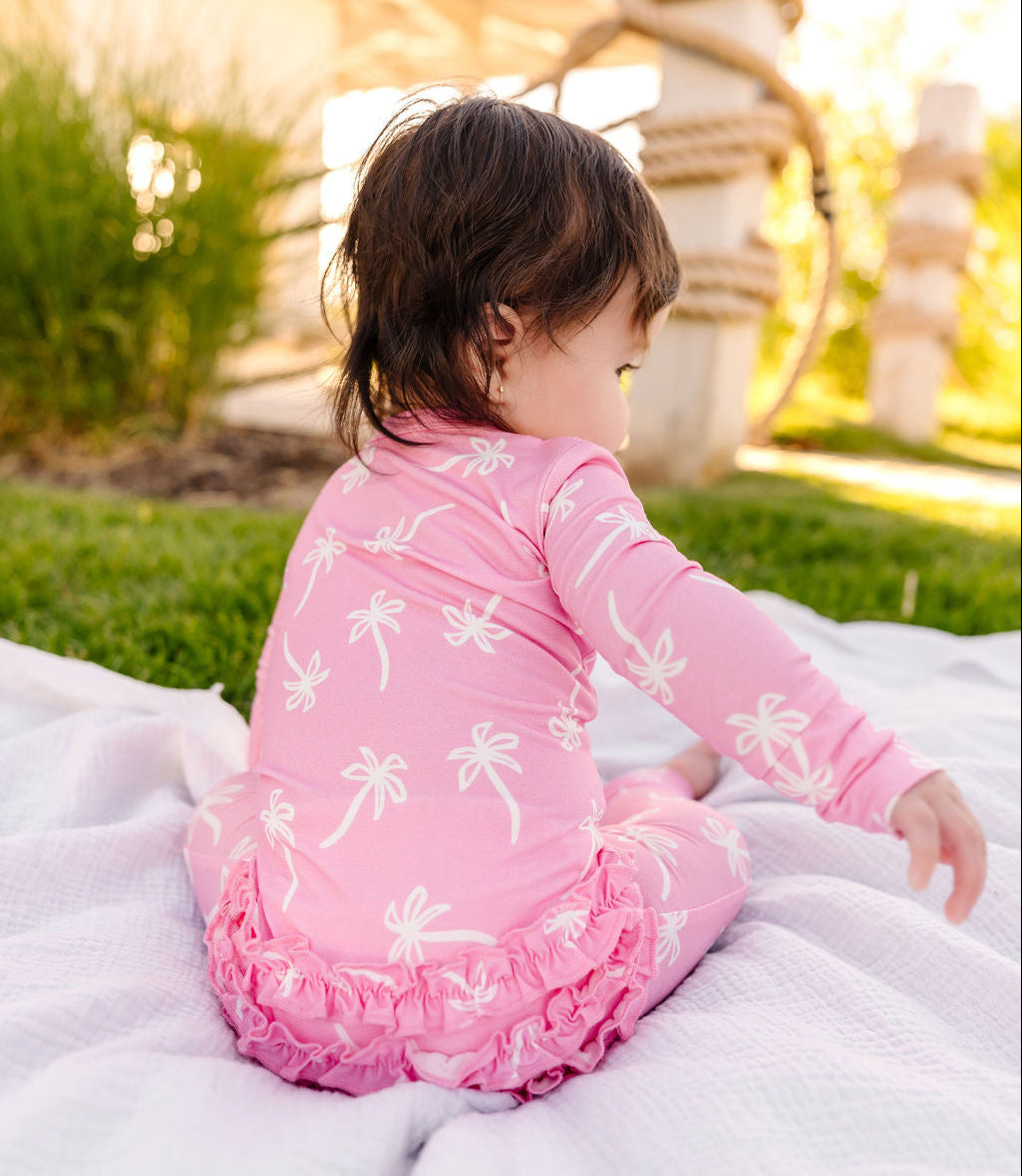 Child in a pink outfit with white patterns sitting on a blanket outdoors.
