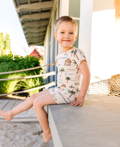 Child wearing a tropical-themed pj set sitting on a ledge outdoors.