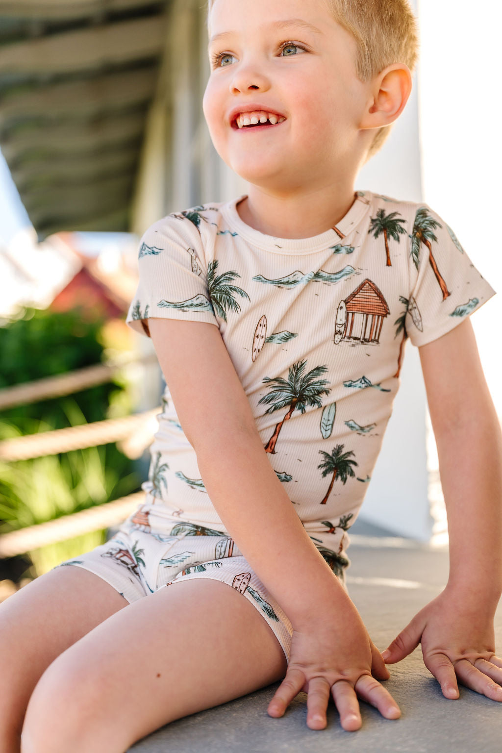 Child wearing a tropical-themed outfit with palm trees and beach huts, sitting outdoors.