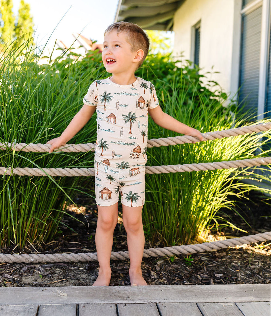 Child wearing a patterned pajama set standing on a wooden deck with greenery in the background
