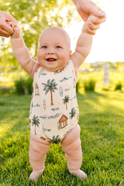 Baby standing on grass wearing a palm tree-themed romper