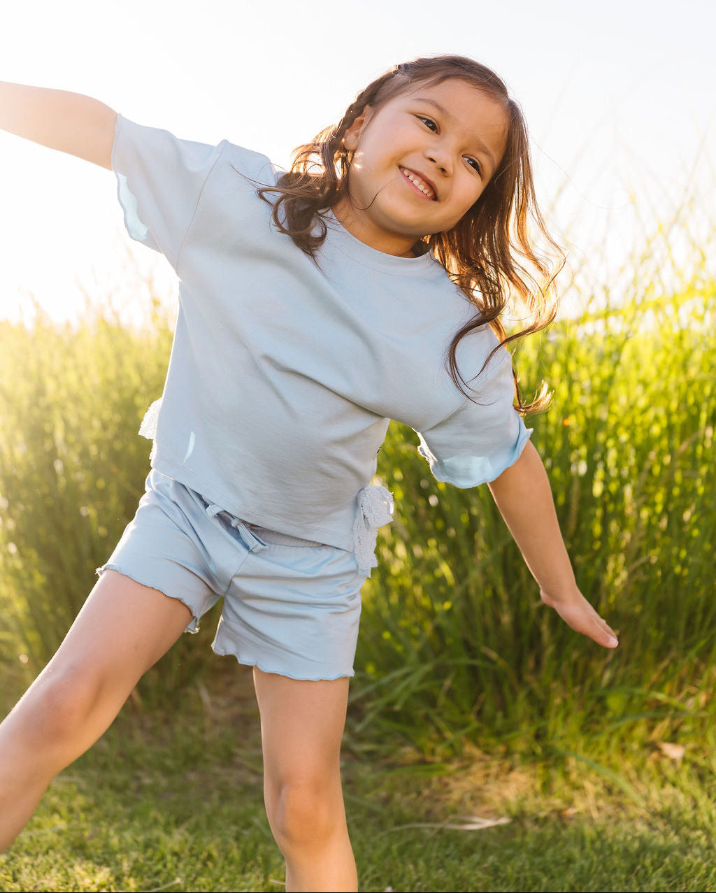 Child in light blue outfit playing outdoors with green grass and sunlight
