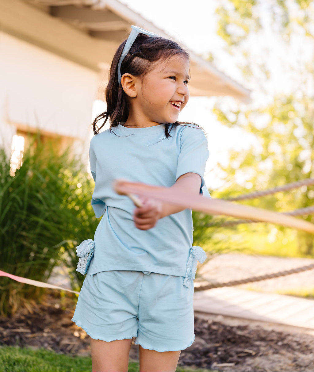 Young girl in light blue outfit standing outdoors with a blurred background