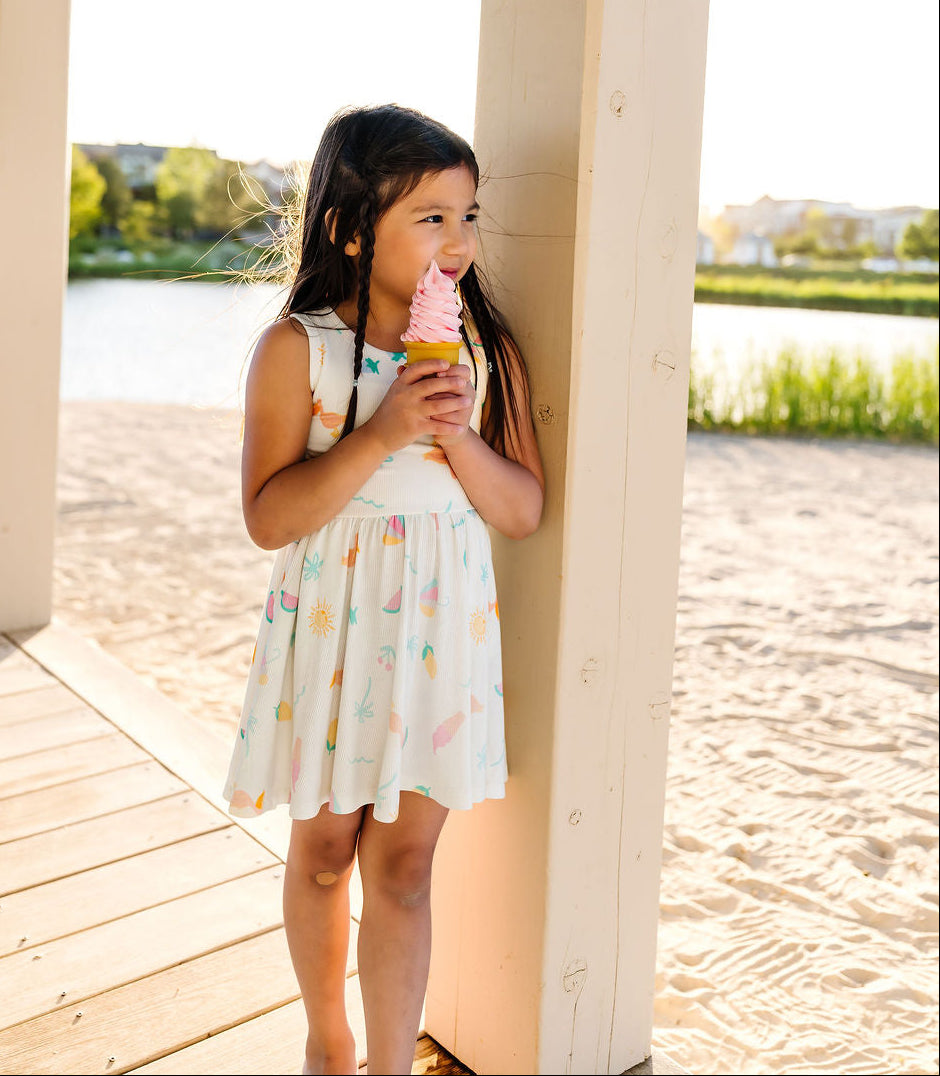 Young girl in a white dress with colorful patterns standing under a gazebo, holding an ice cream cone.