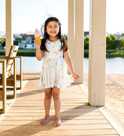 Young girl standing on a wooden deck by a lake, holding a drink.