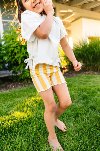 Child in yellow striped shorts and white top playing on grass