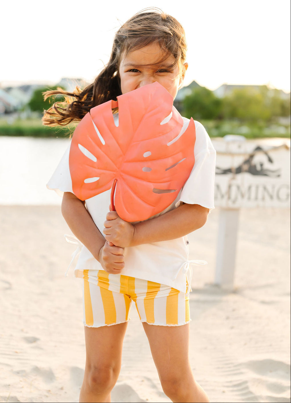 Child holding a large pink leaf-shaped toy on a beach