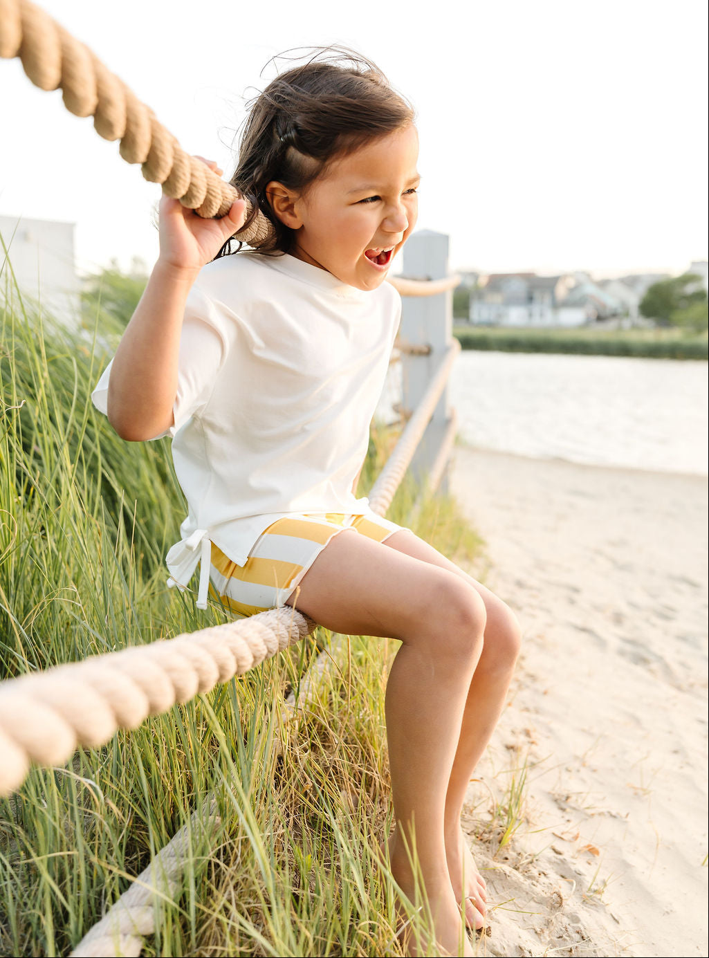 Child sitting on a rope swing in a grassy area with a beach in the background