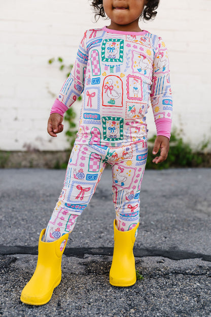 Child wearing a colorful patterned outfit with yellow rain boots on a concrete surface.
