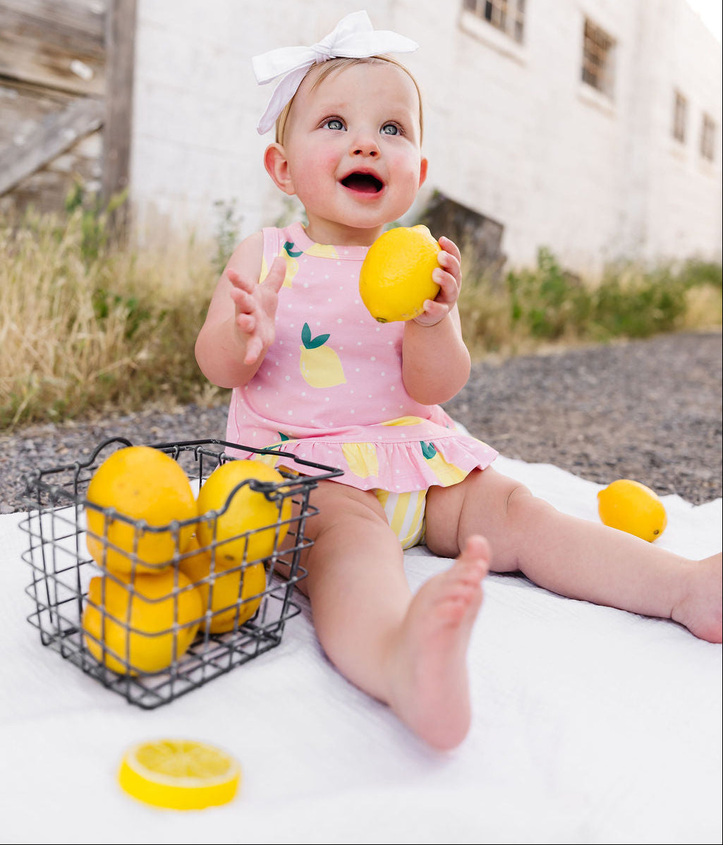 Baby holding a lemon with a basket of lemons on a white blanket