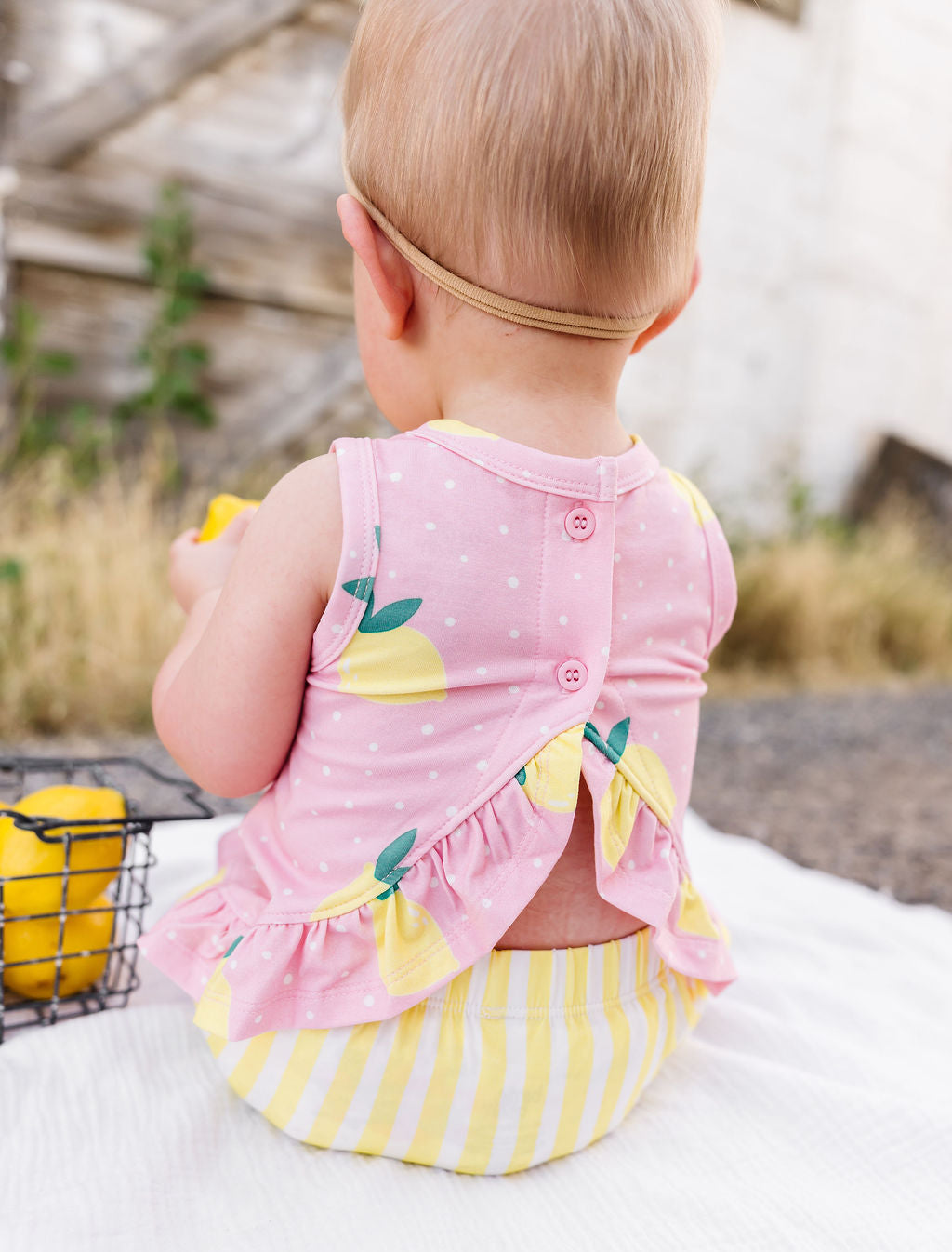 Baby wearing a pink and yellow outfit with lemon design outdoors.