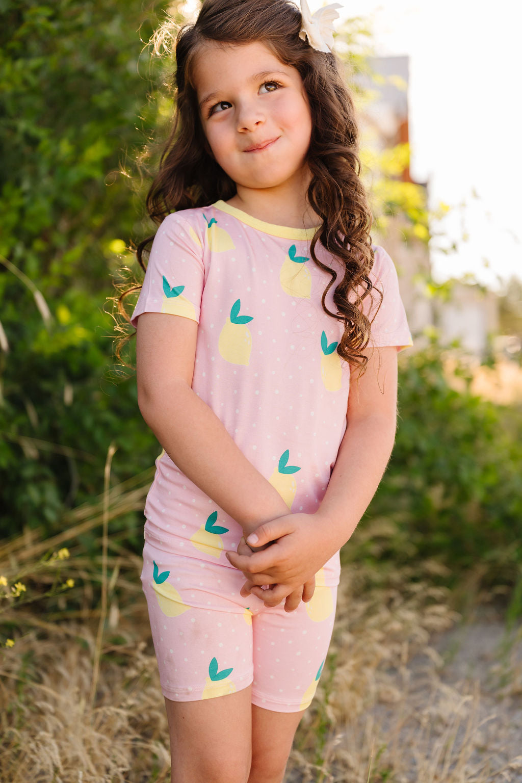 Young girl wearing a pink pajama set with lemons standing outdoors.