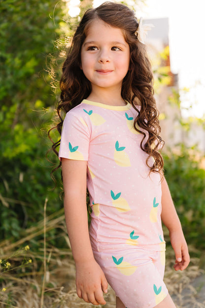 Young girl wearing a pink outfit with lemon patterns outdoors.