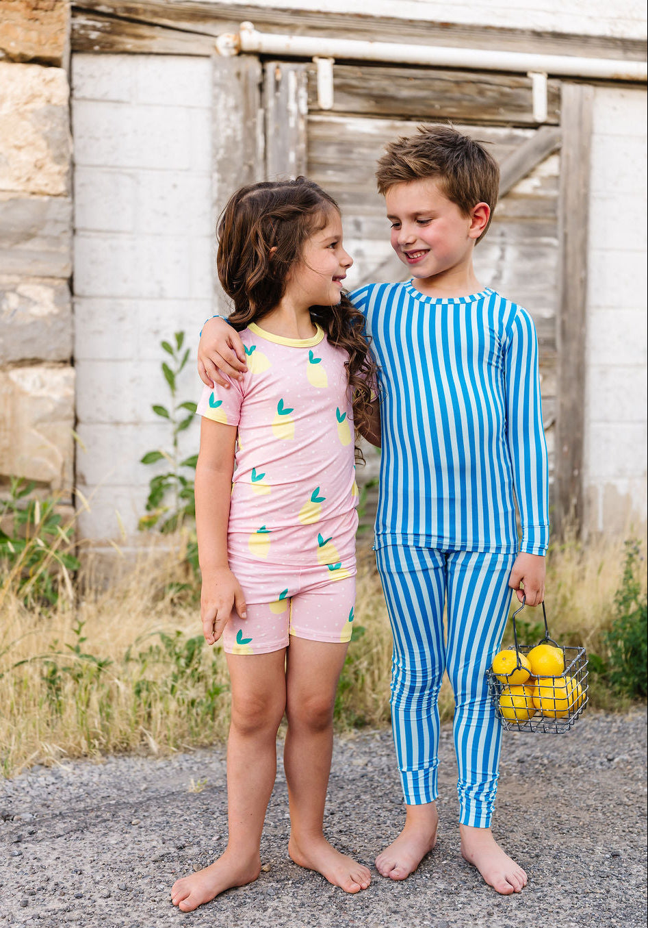 Two children in pajamas standing outdoors near a rustic wooden building.