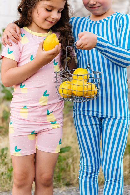 Two children in colorful pajamas holding lemons and a wire basket.