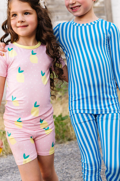 Two children wearing matching pajama sets with lemon pattern and blue striped design.
