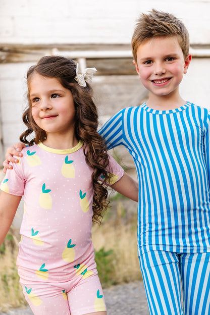 Two children in pajamas standing outdoors with a wooden fence in the background.